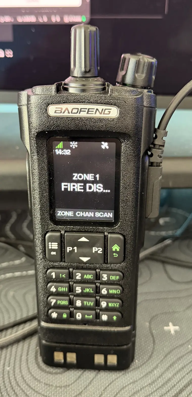A Baofeng UV-32 handheld running tRadio's firmware, its screen showing ZONE 1, FIRE DIS… and a ZONE / CHAN / SCAN softkey row